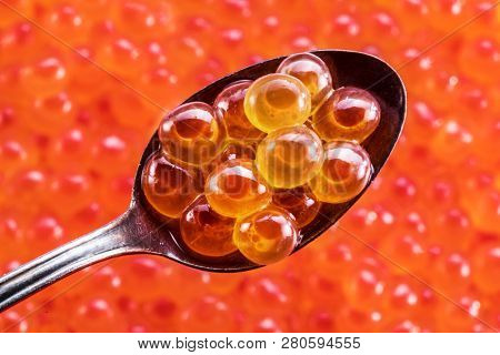 Salmon roe in the silver spoon close-up. Red caviar at the background.