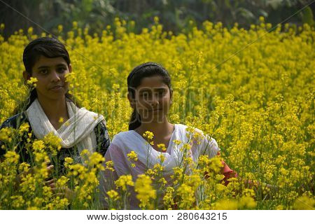 Two Beautiful Asian Teens Standing In A Mustard, Rape Field With Yellow Color Flowers, Covering Head