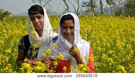 Two Beautiful Asian Teens Standing In A Mustard, Rape Field With Yellow Color Flowers, Covering Head