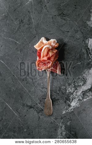 Antipasto Meat Assorti Of Sliced Jamon, Salami, Chorizo Sausage On Fork Over Black Marble Background
