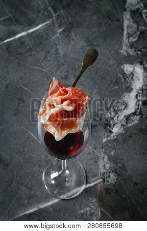 Antipasto Meat Assorti Of Sliced Jamon, Salami, Chorizo Sausage On Fork Under Glass Of Red Wine Over