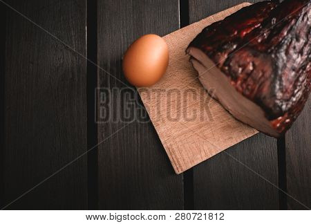 Photo (from Above) Of Smoked Meat With Egg On Dark Wooden Background. Illuminated Meal On Wooden Taa