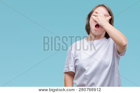 Young adult woman with down syndrome over isolated background peeking in shock covering face and eyes with hand, looking through fingers with embarrassed expression.