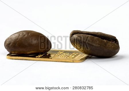 Two Roasted Coffee Beans On A Small Ingot Of 999.9 Gold. Isolated On White. Macro Photography. Selec