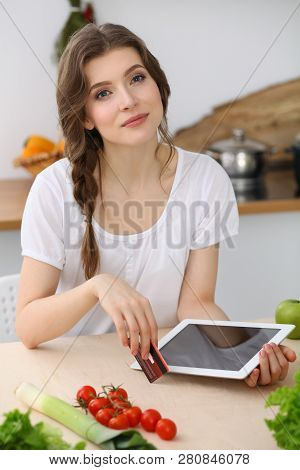 Young  Woman Looking For A New Recipe For  Cooking In A Kitchen. Housewife Is Making Online Shopping