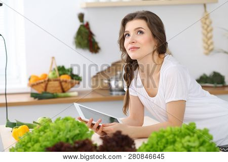 Young  Woman Looking For A New Recipe For  Cooking In A Kitchen. Housewife Is Making Online Shopping