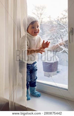 Boy In A White Sweater Standing At The Window On The Windowsill