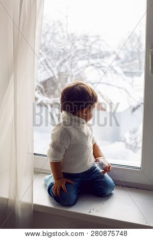 Boy In A White Sweater Standing At The Window On The Windowsill