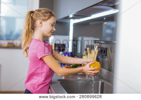 Long-haired Pretty Girl In A Pink Shirt Washing Vegetables In The Kitchen
