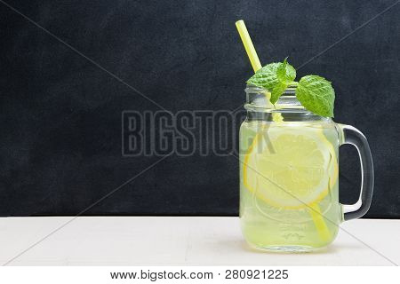Mason Jar Glass Of Lemon Lemonade With Lemons And Straw On Table And Wooden Background. Cold Summer 