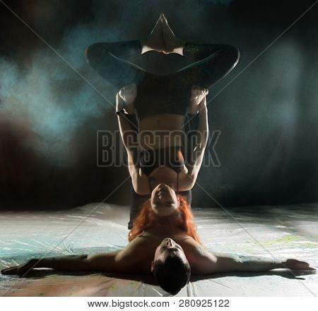 Sports Man And Woman Doing Acroyoga Exercises In A Dark Room With Colorful Smoke