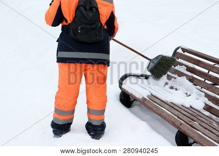 Snow Removal, Municipal Worker With A Broom Clears Snow In Winter. Woman In Uniform Sweeps Snow From