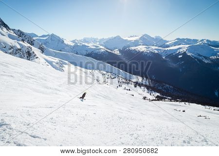 Snowboarder On A Hill At The Top Of Blackcomb, 7th Heaven, With A View Looking Toward Whistler On A 