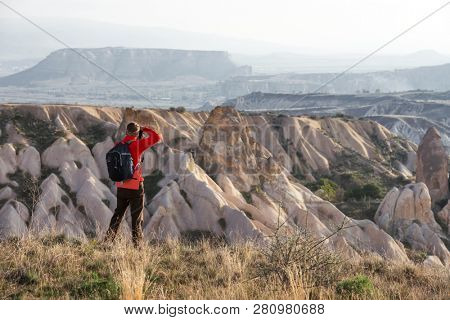 Amazing day in Cappadocia mountains, Turkey. Photographer in red jacket taking photo of amazing hills. Landscape photography