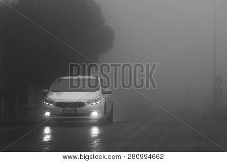 Adrano, Catania Italy - 01 18 2019: A White Car With White Lights On The Wet Road In The Fog. Black 