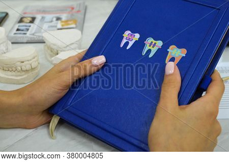 Orthodontist Doctor Holding His Blue Diary With Braces On The Cover