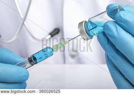 A Doctor In White Coat Drawing Clear Light Blue Liquid From A Vial Into A Syringe. Medication Or Vac