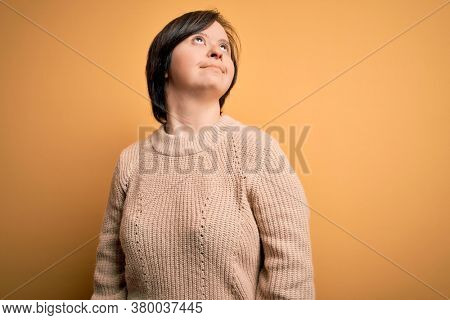 Young down syndrome woman wearing casual sweater over yellow background looking away to side with smile on face, natural expression. Laughing confident.