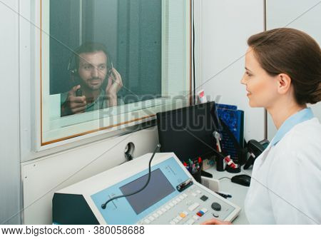 Audiologist Woman Doing The Hearing Exam To A Mixed-race Man Patient Using An Audiometer In A Specia