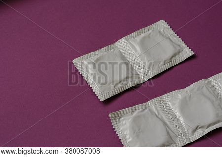Four Condoms Packaged On Purple Background. Fertility Control. Protection Against Sexually Transmitt