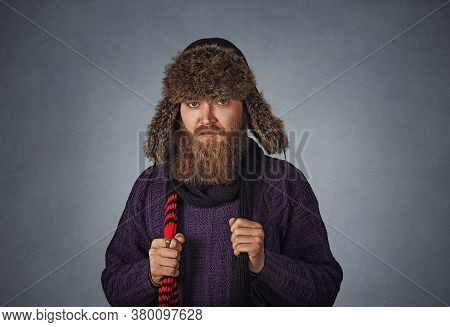 Bearded Serious Male Man In Fluffy Russian Fur Hat Cap Dressed In A Pullover Sweater Holding Red Sca