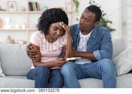 Infertility Concept. African Sad Man Hugging His Upset Wife, Got Negative Pregnancy Test, Home Inter