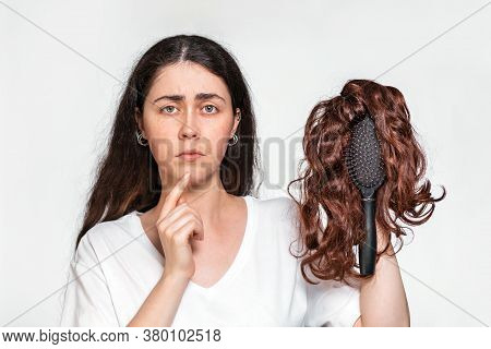 Portrait Of A Sad Woman Holds A Comb With A Wig On It. White Background. Concept Of Hair Care And Ha