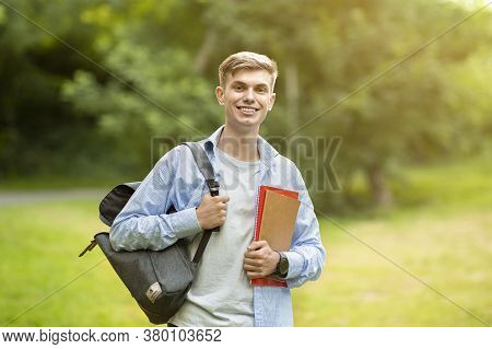 Handsome University Student Guy With Backpack And Workbooks Posing Outdoors At Campus Cortyard, Smil