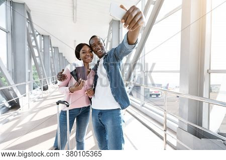 Vacation Selfie. Happy African American Couple Taking Photo On Smartphone In Airport, Posing Togethe