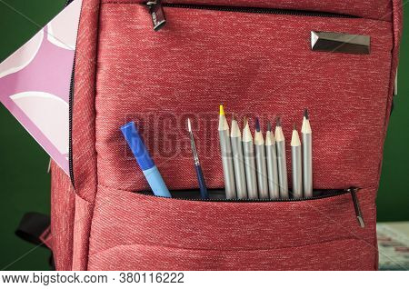 Colored Pencils, A Paintbrush, And A Blue Pen Look Out Of A School Bag Pocket. Preparing For School.
