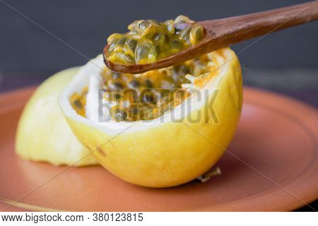 Passion Fruit Cut In Half, Ready To Be Eaten With Wooden Spoon, On Brown Plate, Against Black Backgr
