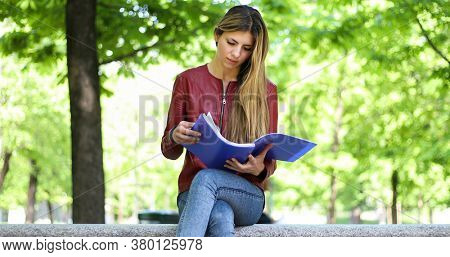 Beautiful female college student reading a book on a bench in a park