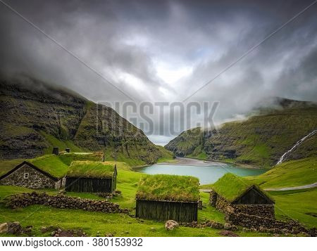 Small Houses Near A Blue Lake, A Small House Made Of Stones With Covered Grass On The Shore Of A Bea