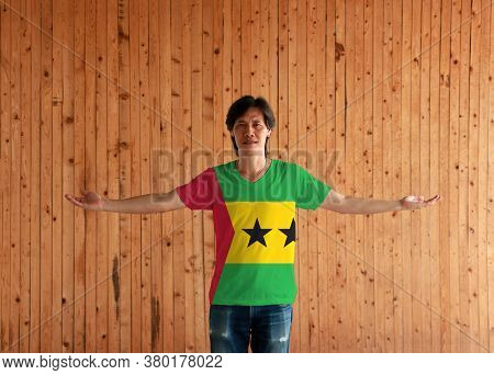 Man Wearing Sao Tome And Principe Flag Color Shirt And Standing With Arms Wide Open On The Wooden Wa