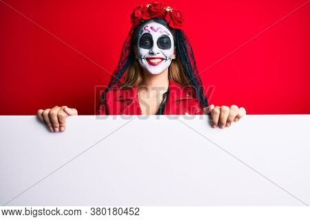 Woman wearing day of the dead costume holding blank empty banner looking positive and happy standing and smiling with a confident smile showing teeth 