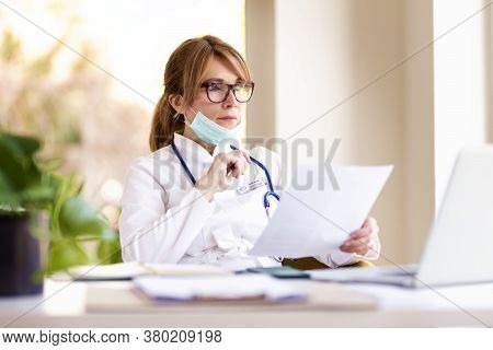 Shot Of Careworn Female Doctor Wearing Face Mask For Prevention While Sitting At Desk And Working On