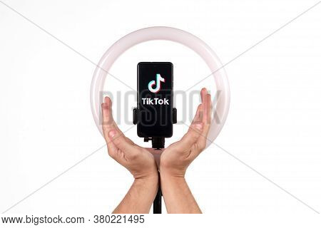 The Tiktok Logo On A Smartphone Attached To A Round Lamp With A Tripod And Male Hands Show Protectio