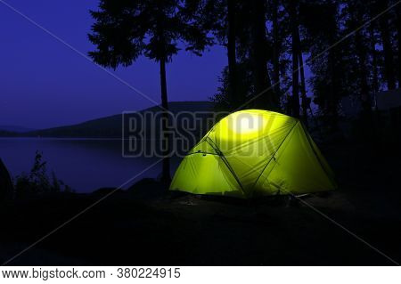 The Tent Glows In The Night. Camping By The Lake In A Pine Forest. Romantic Trip.