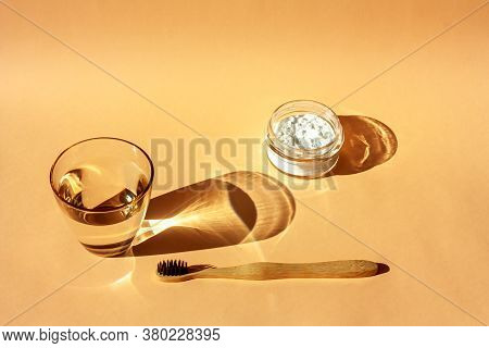Bamboo Toothbrush, Glass Of Water And Toothpaste Powder On A Peach-colored Pastel Background. Biodeg