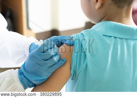 The Doctor Is Using A Syringe To Vaccinate The Asian Child's Shoulder In Hospital. Virus Protection 