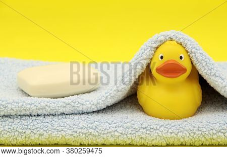 Yellow Rubber Toy Cute Duckling On A Soft Blue Towel With Scented Baby Bathroom Soap On A Yellow Bac