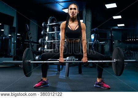 Front View Of Female Bodybuilder With Braids Holding Barbell In Plie Squat. Srtong Woman With Muscul