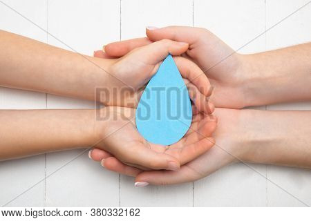 Human Hands Holding Water Drop Isolated On White Wooden Background. Top View. Eco Friendly Living, H