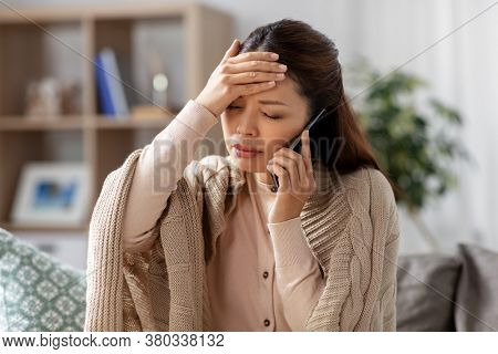 technology, health and cold concept - sick asian woman having headache calling on smartphone at home