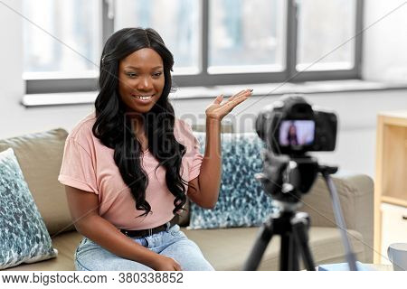 blogging, videoblog and people concept - happy smiling african american female video blogger with camera videoblogging at home