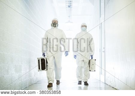 Corona virus concept. Two male scientist doctors in biochemical protective suits walk in laboratory coridor with biohazard analysis cases. Getting ready for COVID pandemic outbreak quarantine.