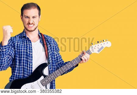 Young handsome caucasian man playing electric guitar annoyed and frustrated shouting with anger, yelling crazy with anger and hand raised 