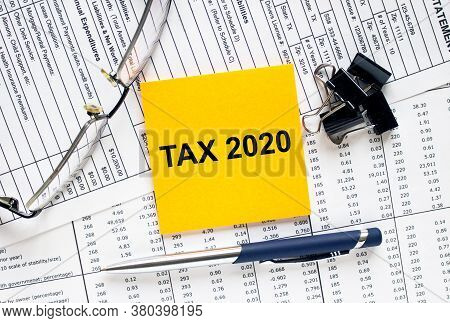 Text Tax 2020 On Financial Tables With Pen, Glasses And Paper Clips