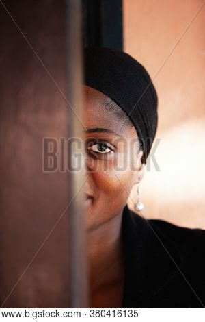 smiley shy African woman dressed in black clothes peeping behind the door