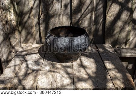 Vintage Cast-iron Pot Of Black Color On Wooden Boards On A Sunny Day Outdoor. Cooking Food.